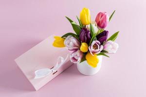 uma ramalhete do Primavera flores dentro uma branco vaso Próximo para uma presente caixa com uma fita. Rosa fundo. a conceito do uma presente e uma Boa humor. foto