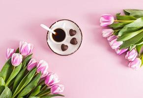 Primavera lilás tulipas e uma copo do aromático café em uma pires com em forma de coração chocolates. festivo fundo. uma cópia de do a espaço. foto