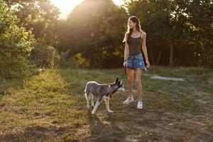 mulher e dela rouco cachorro caminhando alegremente em a Relva dentro a parque sorrir com dentes dentro a outono andar com dela bicho de estimação, viagem com uma cachorro amigo foto
