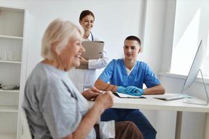 alegre idosos mulher dentro a hospital falando para uma enfermeira e uma médico consulta foto