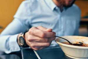 uma homem come borscht com azedo creme dentro uma restaurante às uma mesa dentro uma cafeteria e uma Assistir em dele mão foto