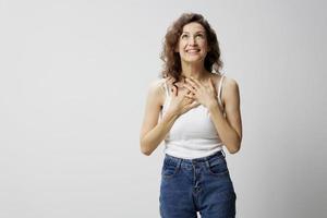 muito feliz chocado surpreso feliz encaracolado lindo mulher dentro básico branco camiseta dobra mãos em peito posando isolado em sobre branco fundo. pessoas emoções estilo de vida conceito. cópia de espaço foto