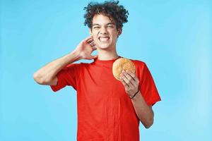 cara com encaracolado cabelo dentro uma vermelho camiseta com uma Hamburger dentro dele mãos velozes Comida dieta foto