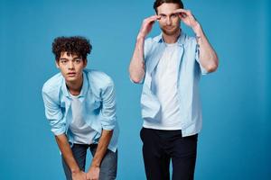 cabelo encaracolado cara dentro uma azul camisa inclinou-se frente e uma loiro homem em uma azul fundo amigos foto