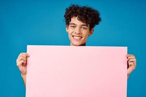 homem com encaracolado cabelo segurando Rosa poster bandeira azul fundo foto