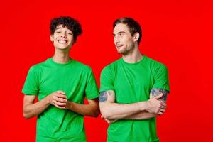 dois alegre amigos dentro verde Camisetas comunicando emoções vermelho fundo foto