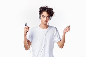 engraçado cara com encaracolado cabelo dentro uma branco camiseta escuta para música tecnologia entretenimento foto