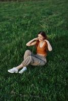 uma mulher desfrutando a ao ar livre sentado dentro a parque em a verde Relva dentro casual roupas com grandes fluindo cabelo, aceso de a brilhante verão Sol sem mosquitos foto