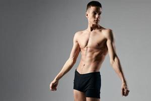 sexy atleta dentro Preto calção em uma cinzento fundo fisiculturista bíceps modelo foto