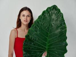 uma mulher dentro uma vermelho camiseta detém uma verde folha dentro dela mão limpar \ limpo pele e uma natural Veja foto