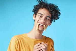 homem com encaracolado cabelo francês fritas dentro dele boca Diversão lanche azul fundo foto