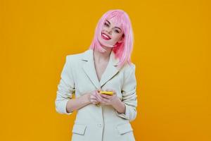 alegre mulher com Rosa cabelo com uma telefone dentro uma branco terno amarelo fundo foto