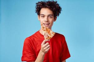 homem segurando uma fatia do pizza dentro dele mão e encaracolado cabelo vermelho camiseta azul fundo foto