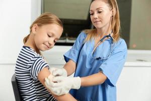 uma mulher médico dentro uma vestir vestido selos uma criança mão com uma gesso foto