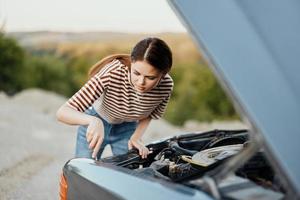 uma mulher viajante carrinhos de dela velho carro com a de capuz aberto e reparos a carro motor com uma chave inglesa, desenroscando carro partes foto