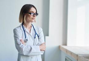 médico mulher dentro uma médico vestido com uma estetoscópio dentro óculos parece Fora a janela foto