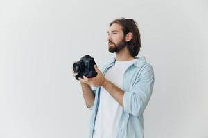 uma masculino hipster fotógrafo dentro uma estúdio contra uma branco fundo parece através a Câmera visor e fotos tiros com natural luz a partir de a janela. estilo de vida trabalhos Como uma freelance fotógrafo