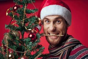 uma homem dentro uma santa chapéu Natal árvore decoração brinquedos vermelho fundo foto