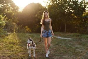 mulher e dela rouco cachorro caminhando alegremente em a Relva dentro a parque sorrir com dentes dentro a outono andar com dela bicho de estimação, viagem com uma cachorro amigo foto