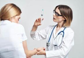 uma mulher detém uma seringa dentro dela mão e uma fêmea paciente dentro uma branco camiseta é assustado modelo foto