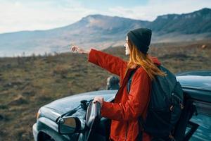 mulher caminhante dentro a montanhas em natureza perto a carro com uma mochila em a costas foto