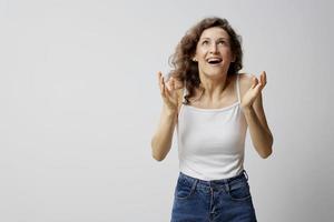 alegre surpreso animado encaracolado lindo mulher dentro básico branco camiseta levantar mãos acima Ganhou uma milhão posando isolado em sobre branco fundo. pessoas emoções estilo de vida conceito. cópia de espaço foto