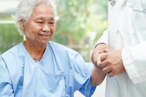 médico de mãos dadas paciente idosa asiática, ajuda e cuidados no hospital. foto