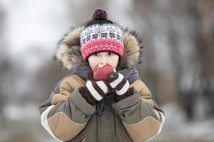 criança dentro a inverno com fruta. Garoto comendo uma vermelho maçã foto