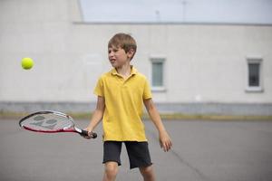 criança com uma tênis raquete e uma bola. Garoto tênis jogador. estudante vai dentro para Esportes foto