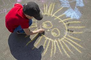 a Garoto desenha com giz em a calçada a sol.infantil rua arte. futuro artista. pequeno picaksso. foto