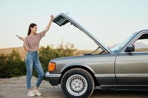 uma mulher carrinhos lado de fora uma quebrado, perigoso velho carro com uma chave inglesa em a estrada viajando sozinho foto