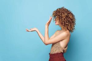 lindo mulher encaracolado cabelo lado Visão mão gestos azul fundo estúdio cópia de espaço foto