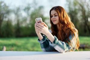 uma jovem fêmea blogueiro senta ao ar livre com dela Smartphone dentro mão e autônomos dentro a ao ar livre. a conceito do uma saudável estilo de vida e trabalhos foto