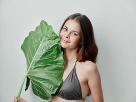 bonita mulher dentro cinzento roupa de banho com verde folha exótico isolado fundo foto