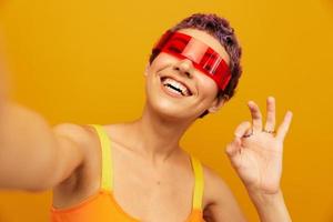 mulher sorridente dentro incomum óculos milenar levando selfies dentro roupa de esporte contra a laranja estúdio pano de fundo, livre espaço foto