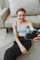 feliz sorrir mulher segurando a velho Câmera e levando As fotos do ela mesma Como uma final de semana fotógrafo dentro casa roupas com uma curto corte de cabelo cabelo sem filtros em uma branco fundo, livre cópia de espaço