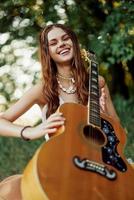 uma jovem hippie mulher com uma guitarra dentro dela mãos sorrisos docemente para dentro a Câmera em uma viagem para natureza estilo de vida dentro harmonia foto