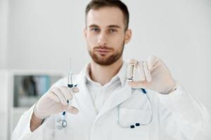 masculino médico dentro uma médico vestido detém uma seringa dentro dele mão vacina saúde Cuidado laboratório químico líquido foto