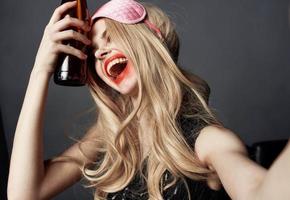 bêbado mulher com uma garrafa do Cerveja tendo Diversão em uma cinzento fundo e gesticulando com dela mãos foto