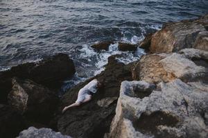 mulher deitado em dela costas em uma rochoso Beira Mar natureza foto