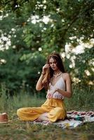 uma jovem hippie mulher medita dentro natureza dentro a parque, sentado dentro uma lótus posição em dela colorida xadrez e desfrutando harmonia com a mundo dentro roupas ecológicas dentro a outono foto