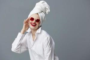 retrato do uma mulher vermelho oculos de sol cosméticos com toalha em cabeça cinzento fundo foto