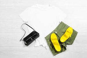 branco fêmea t camisa zombar acima plano deitar em de madeira fundo. verão acessórios. amarelo giro fracassos, bolsa. topo frente Visão camiseta cópia de espaço. brincar camiseta horário de verão. modelo em branco camisa. foto