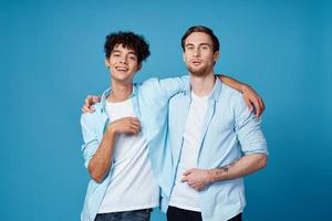 jovem homens dentro azul camisas abraçando em isolado fundo amigos Diversão foto