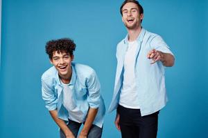 cabelo encaracolado cara dentro uma azul camisa inclinou-se frente e uma loiro homem em uma azul fundo amigos foto