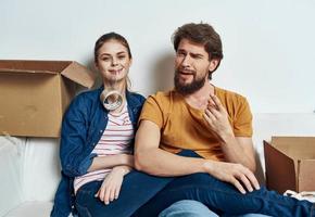 homem e mulher sentado em uma branco sofá dentro uma quarto com caixas do coisas Ferramentas comovente foto