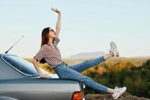 uma mulher com uma carro parado em a estrada para descansar em a viagem elevado dela braços e pernas a partir de felicidade e uma lindo panorama foto