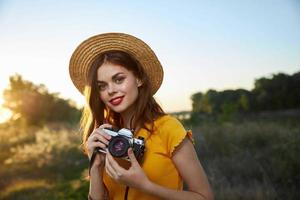 bonita mulher segurando Câmera sorrir vermelho lábios chapéu natureza foto