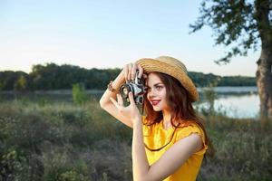 mulher fotógrafo olhando às Câmera com chapéu sorrir vermelho lábios verão fresco ar foto