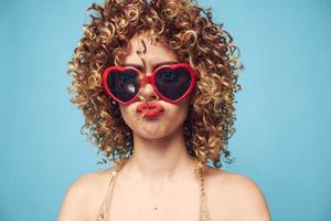 entusiasmado menina festa em uma azul fundo, vermelho oculos de sol foto